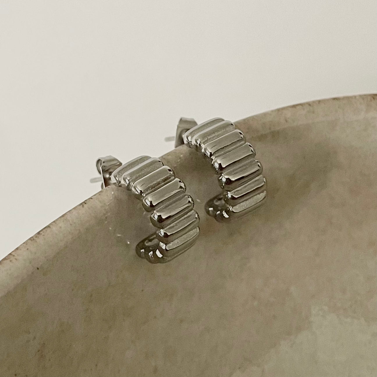 Silver ribbed hoop earrings on a stone surface with a neutral background