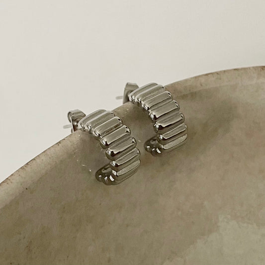 Silver ribbed hoop earrings on a stone surface with a neutral background