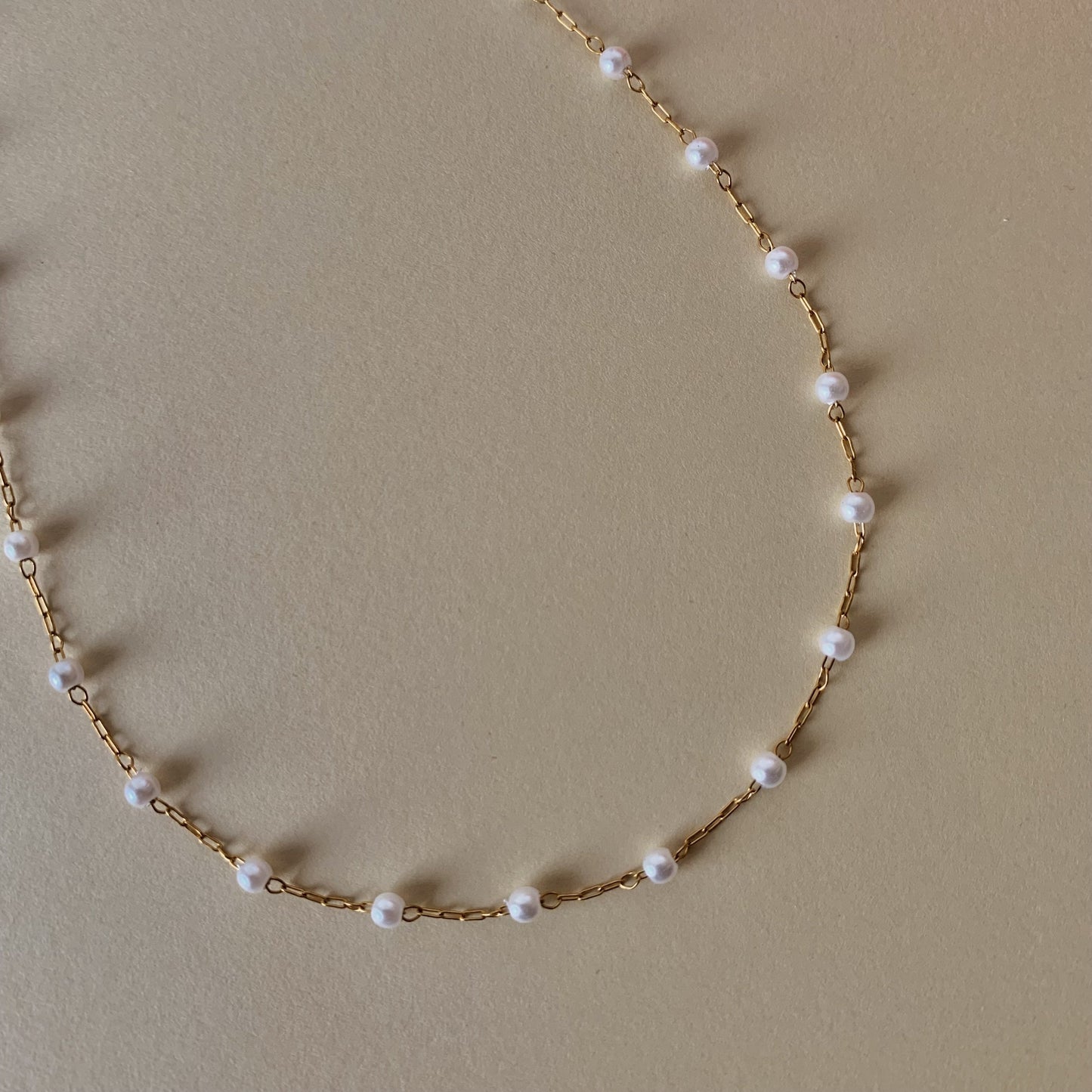 Gold chain necklace with pearls on a beige background