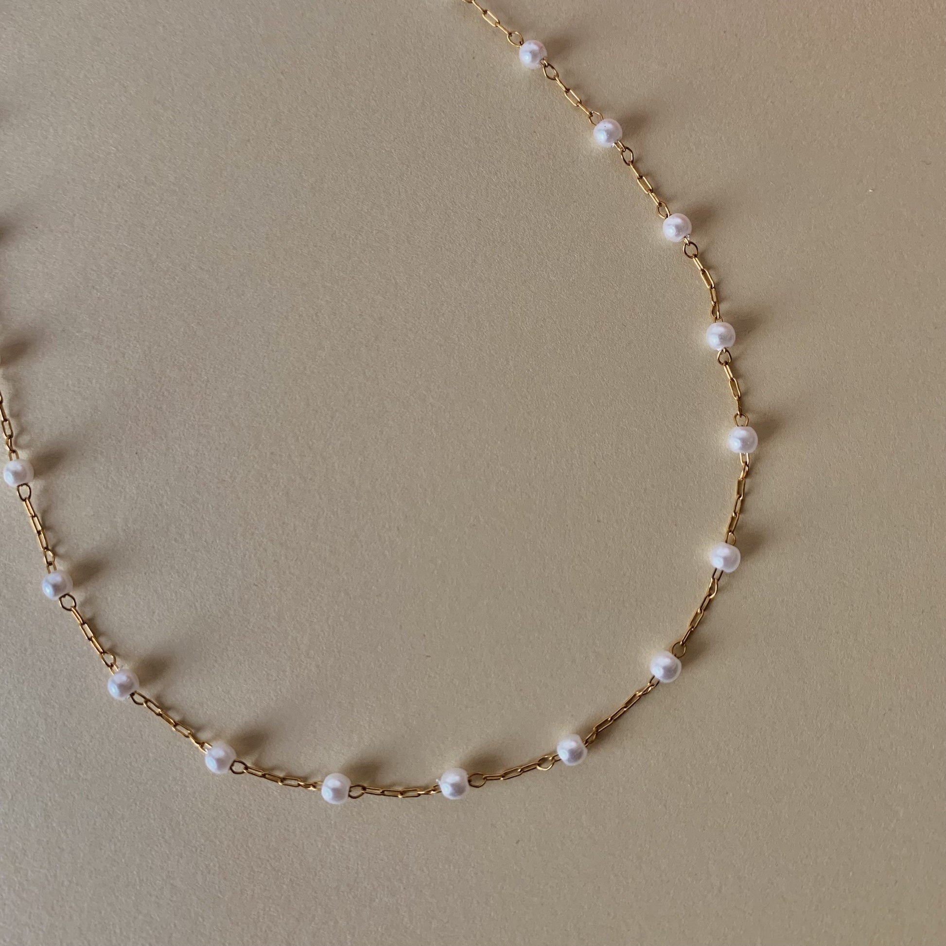 Gold chain necklace with pearls on a beige background