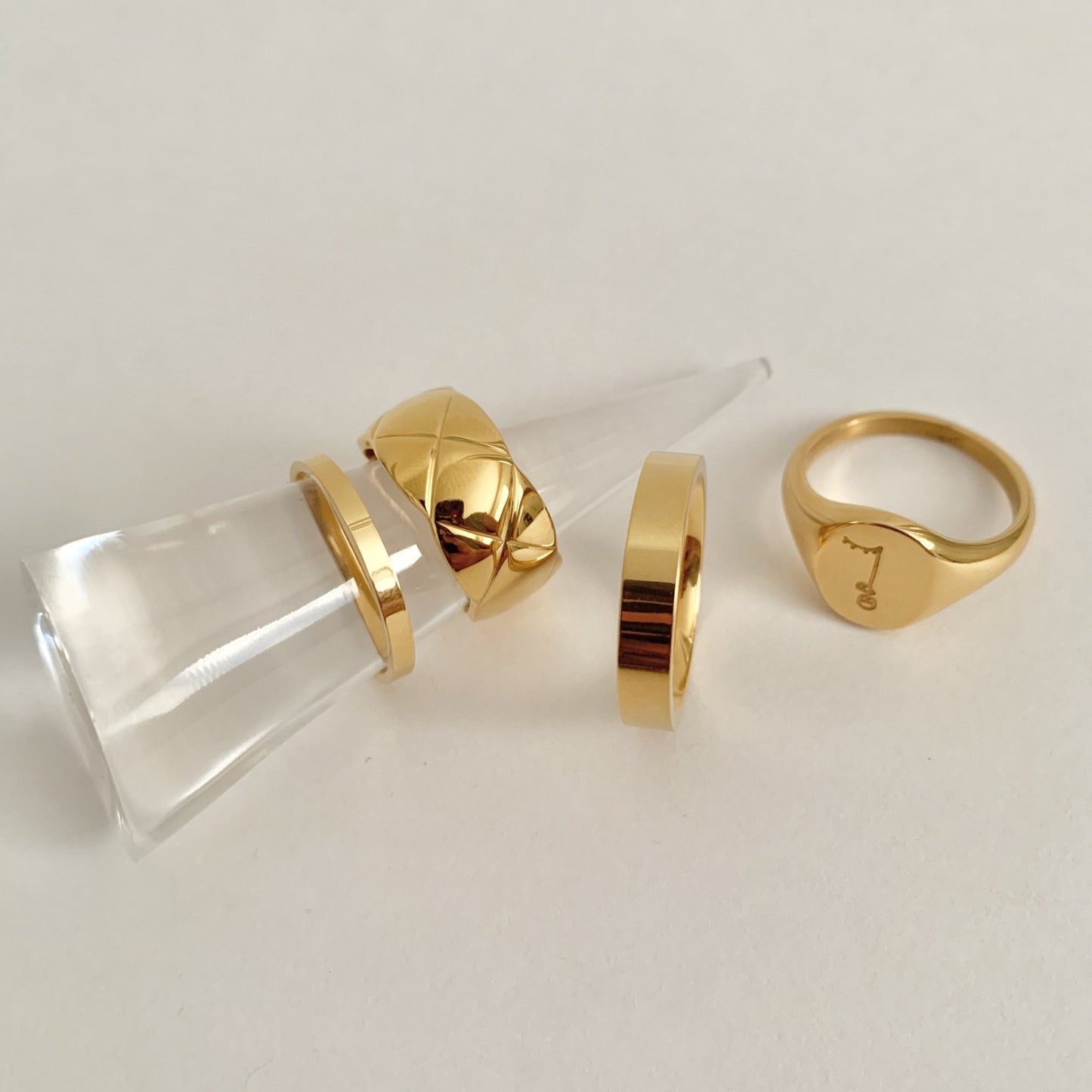 Gold rings displayed on a white surface with a clear cylindrical stand.