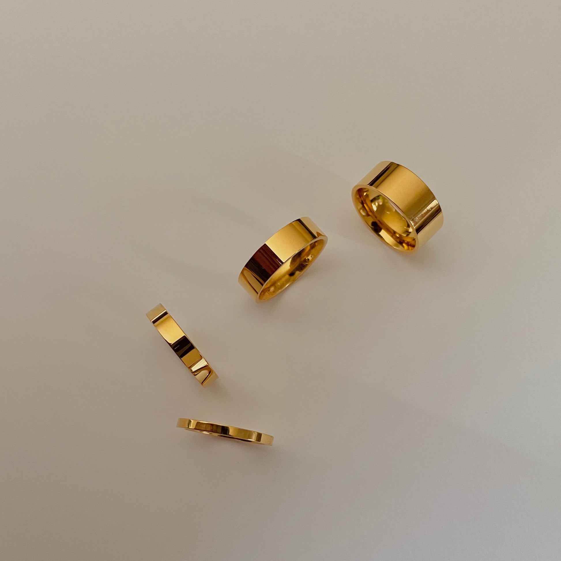 Four gold rings of different thicknesses on a light gray background