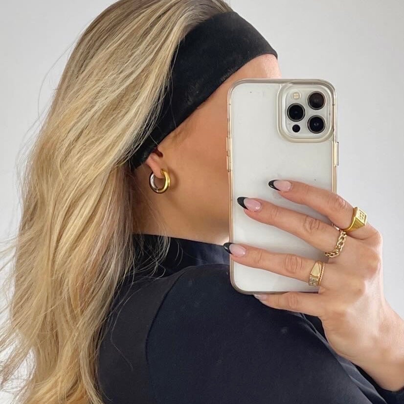 Person holding a phone with a clear case, wearing two toned hoops, on a plain background