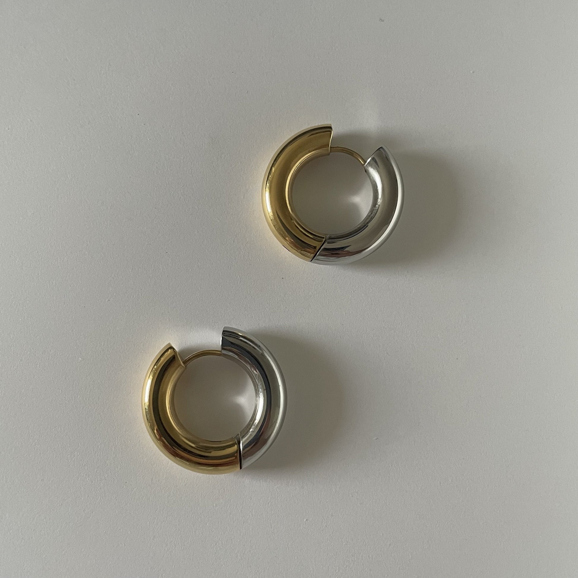 Pair of gold and silver hoop earrings on a light gray background
