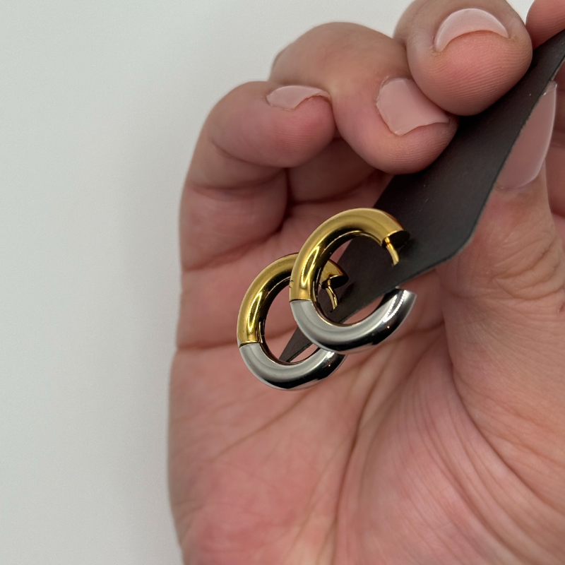 Hand holding half gold and half silver hoops on a white background. Daurielle two tone hoops.