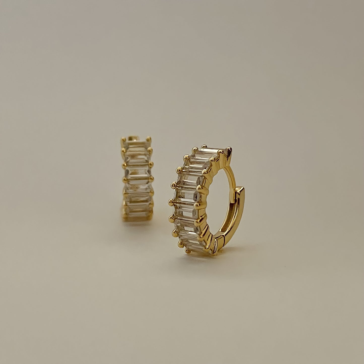 Gold hoop earrings crusted  with clear rectangle gemstones on a beige background.
