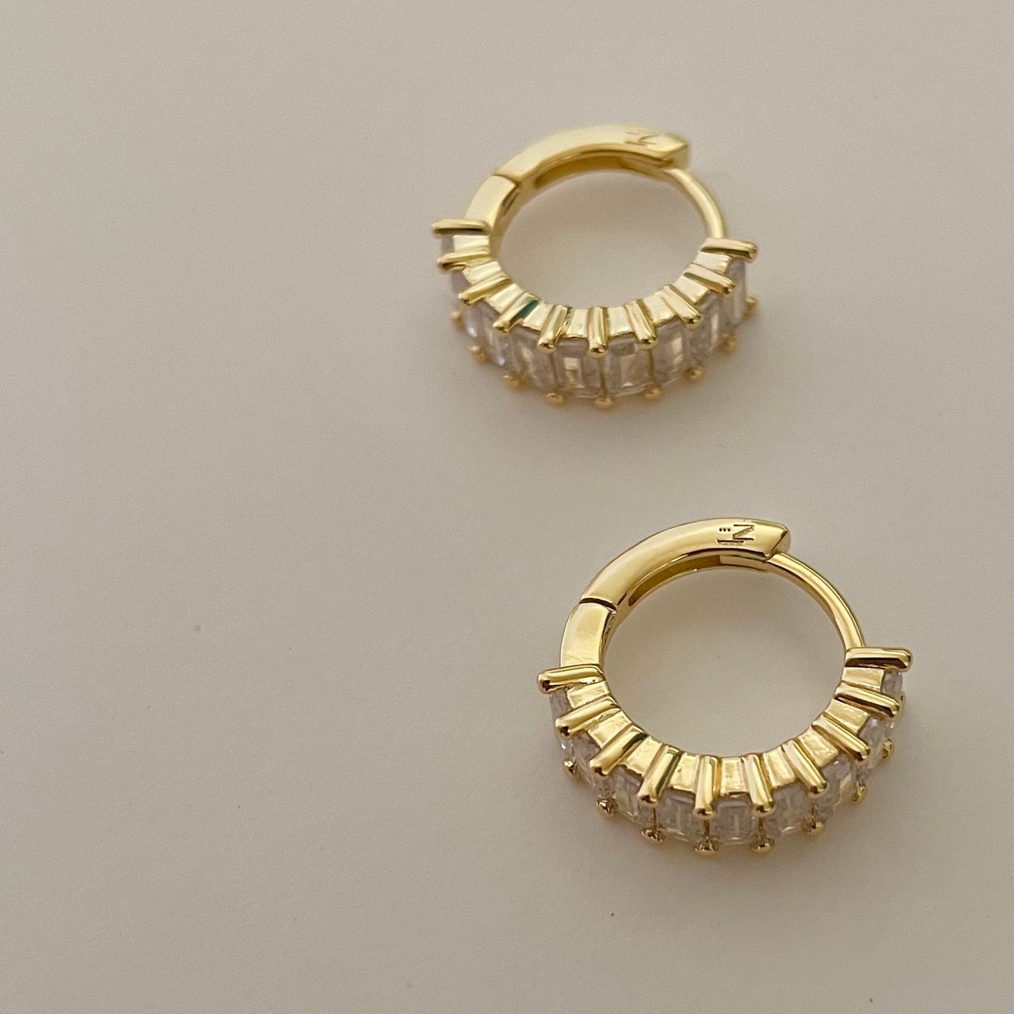 close up gold hoop earrings crusted with clear rectangular gemstones.