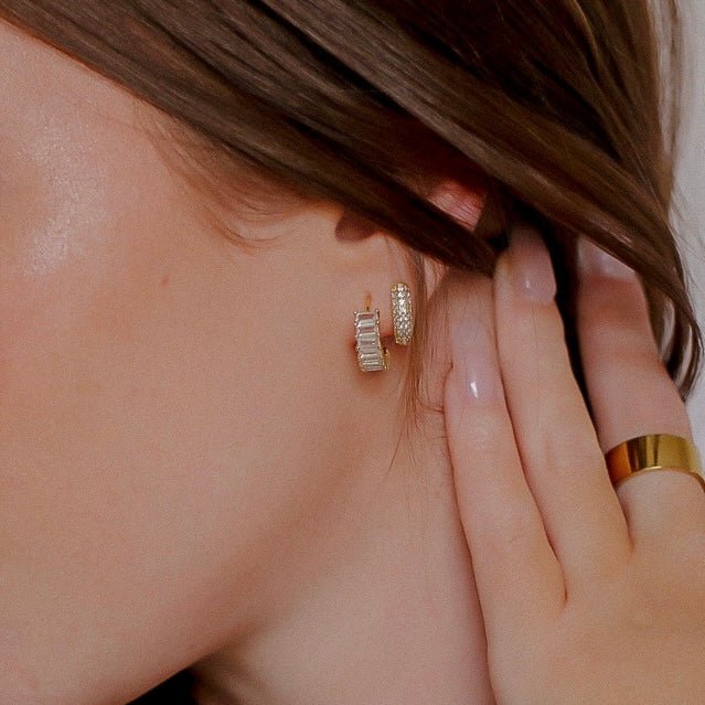 close up of a person wearing gold hoop earrings crusted in clear rectangular gemstones.