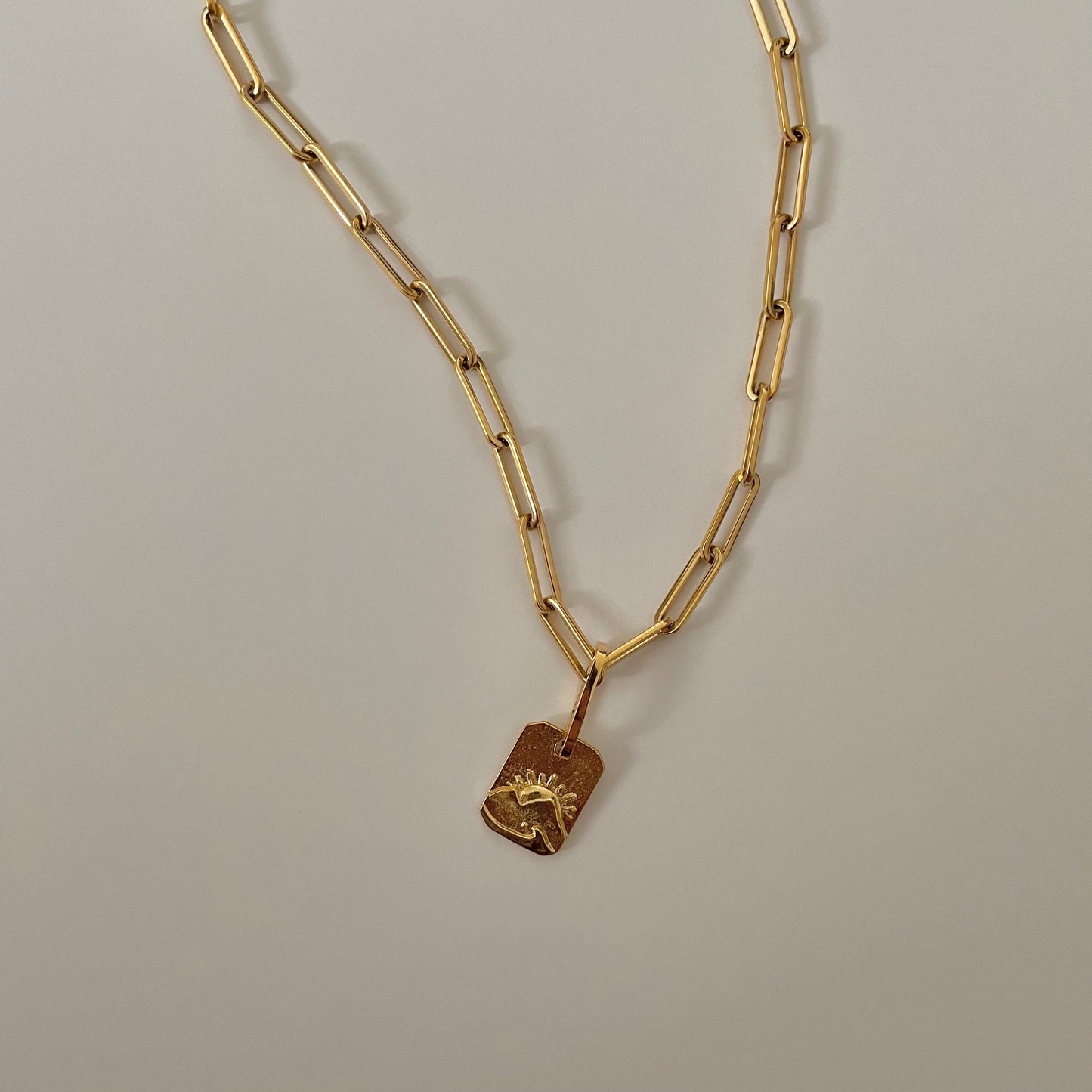 Gold chain necklace with a sunset engraved pendant on a gray background.