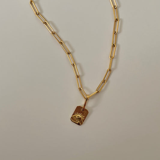 Gold chain necklace with a sunset engraved pendant on a gray background.