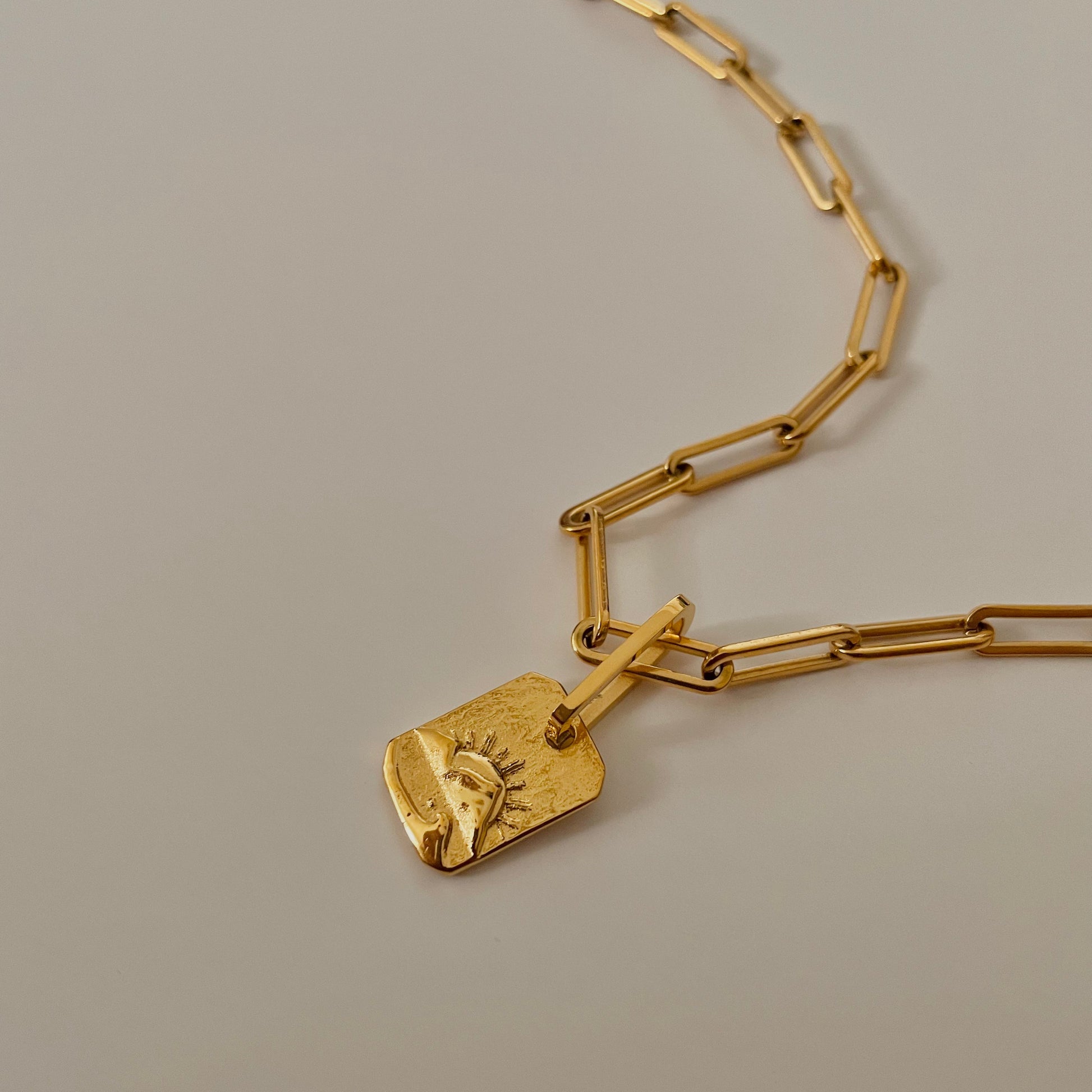 Gold chain necklace with a unique sunset pendant on a beige background