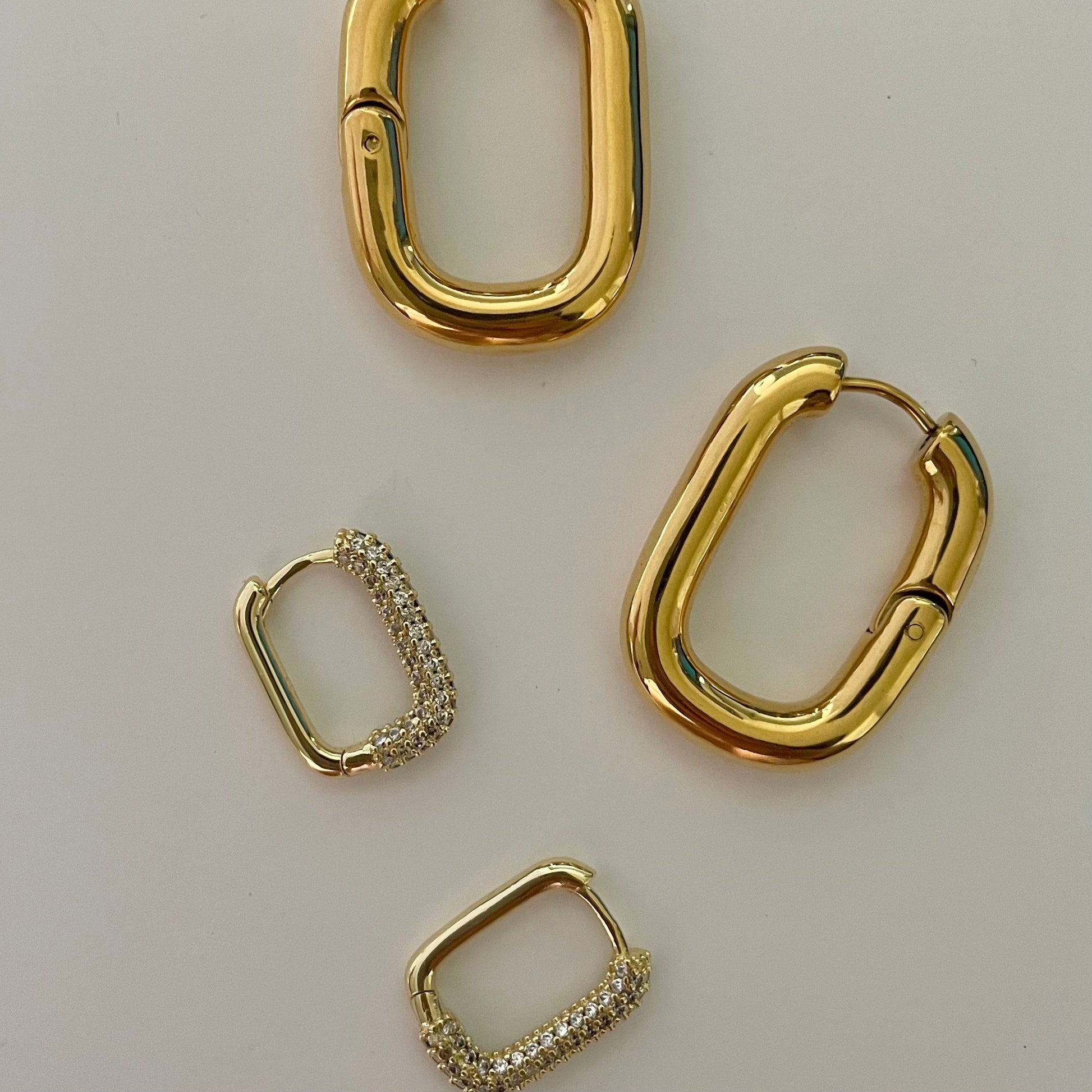 close up gold rectangular hoops with pave crust in comparison to bigger rectangular gold hoops without pave crust.
