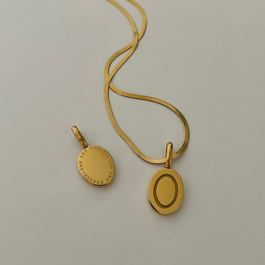 Gold necklace with an oval pendant that reads "you are enough" on a light gray background